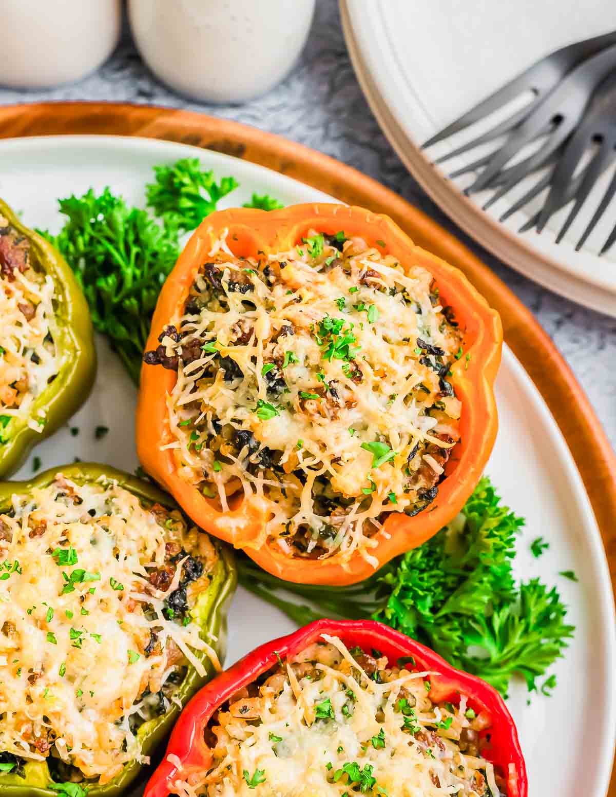 Stuffed bell peppers filled with a mixture of rice, vegetables, and ground sausage, topped with melted cheese, and garnished with chopped parsley, served on a white plate with fresh parsley.