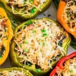 A close-up of colorful sausage stuffed bell peppers topped with melted cheese and garnished with chopped herbs.