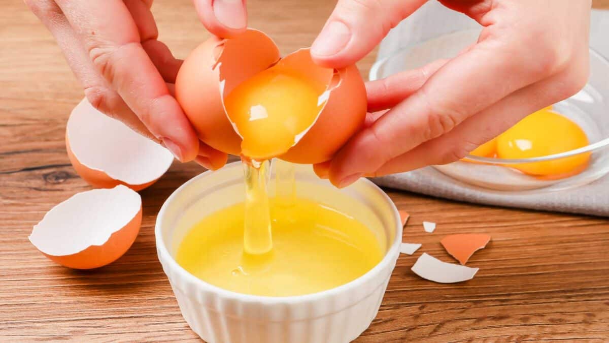 Woman separating egg yolk from white over bowl at wooden table.