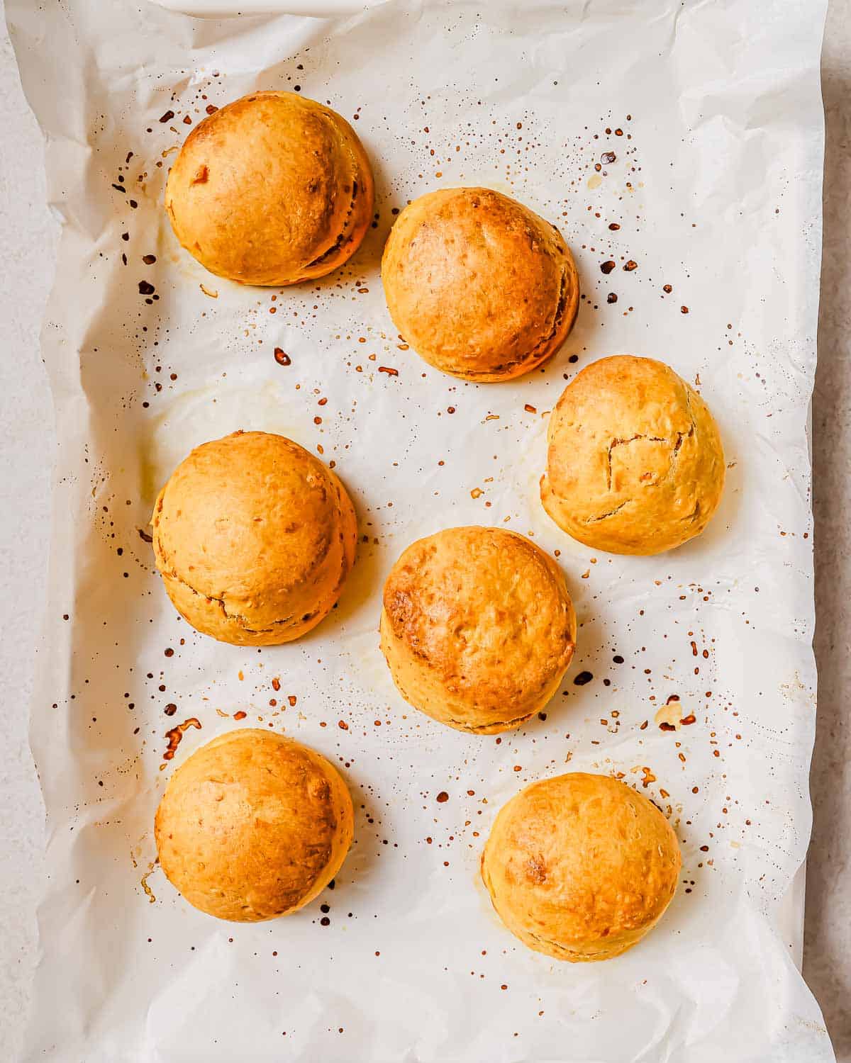 Seven golden-brown baked sweet potato biscuits on a parchment-lined baking sheet.