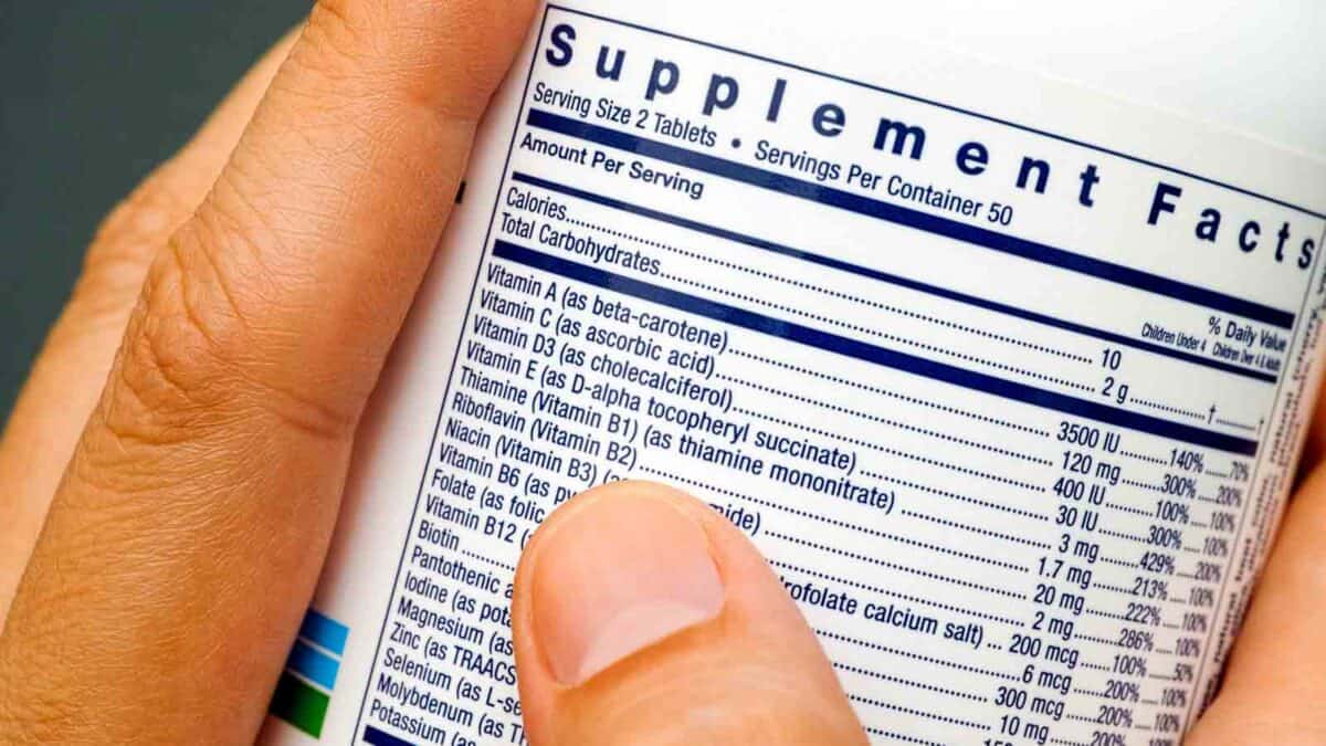 Close-up of hands holding a bottle with a detailed supplement facts label listing vitamins and nutritional information.