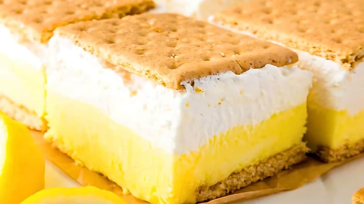 A close-up of layered lemon icebox dessert with graham cracker crust, creamy lemon filling, and whipped topping.