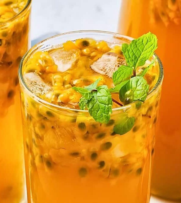 Three glasses filled with fresh passion fruit juice, garnished with mint leaves, and containing ice cubes, are placed on a white surface.