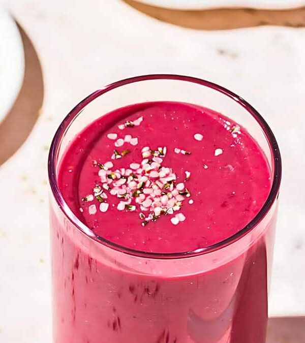 A tall glass filled with a bright pink smoothie, topped with a sprinkling of mixed seeds.