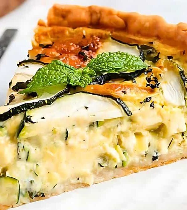 A slice of vegetable quiche on a white plate, garnished with mint leaves, with a fork resting beside it.