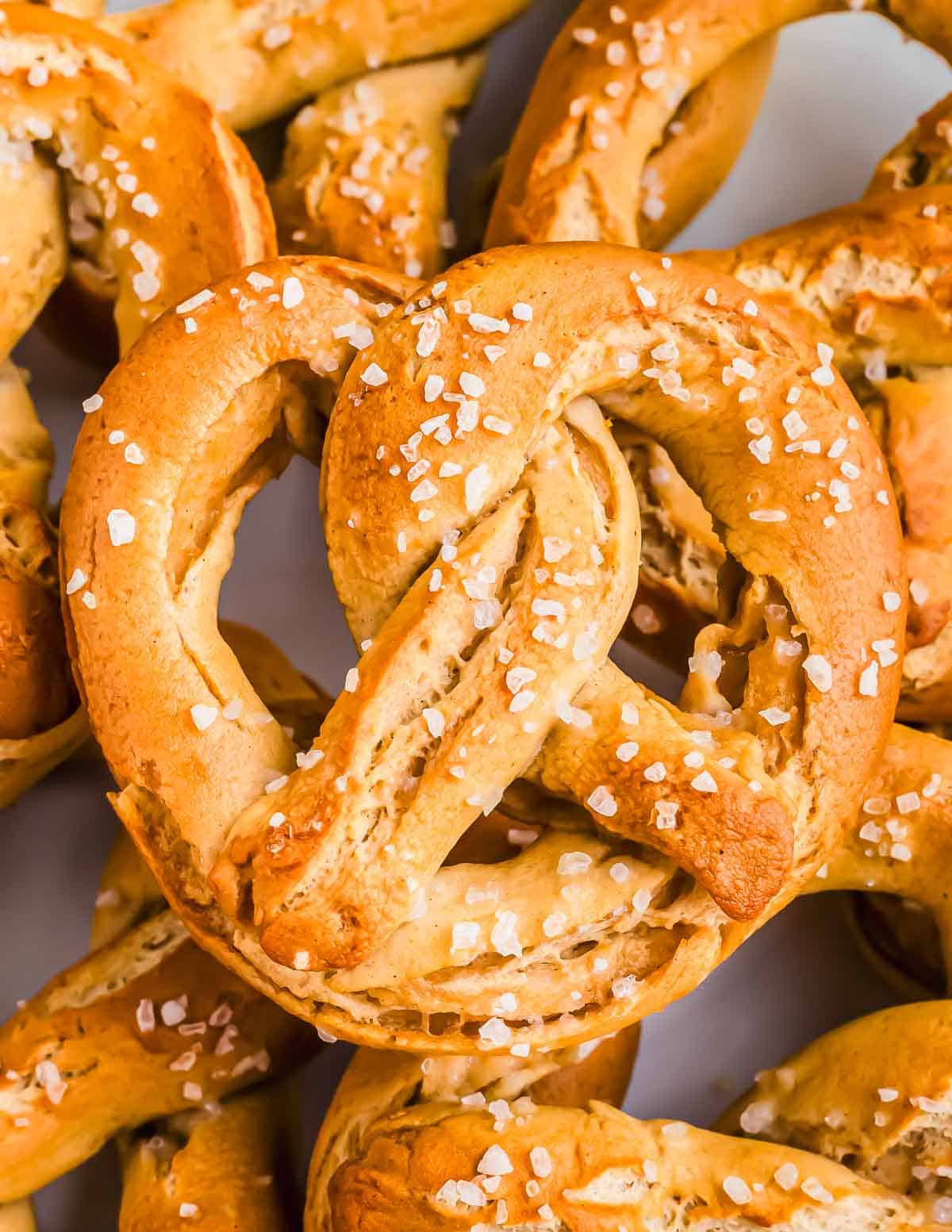 A close-up of several freshly baked soft GF pretzels sprinkled with coarse salt.