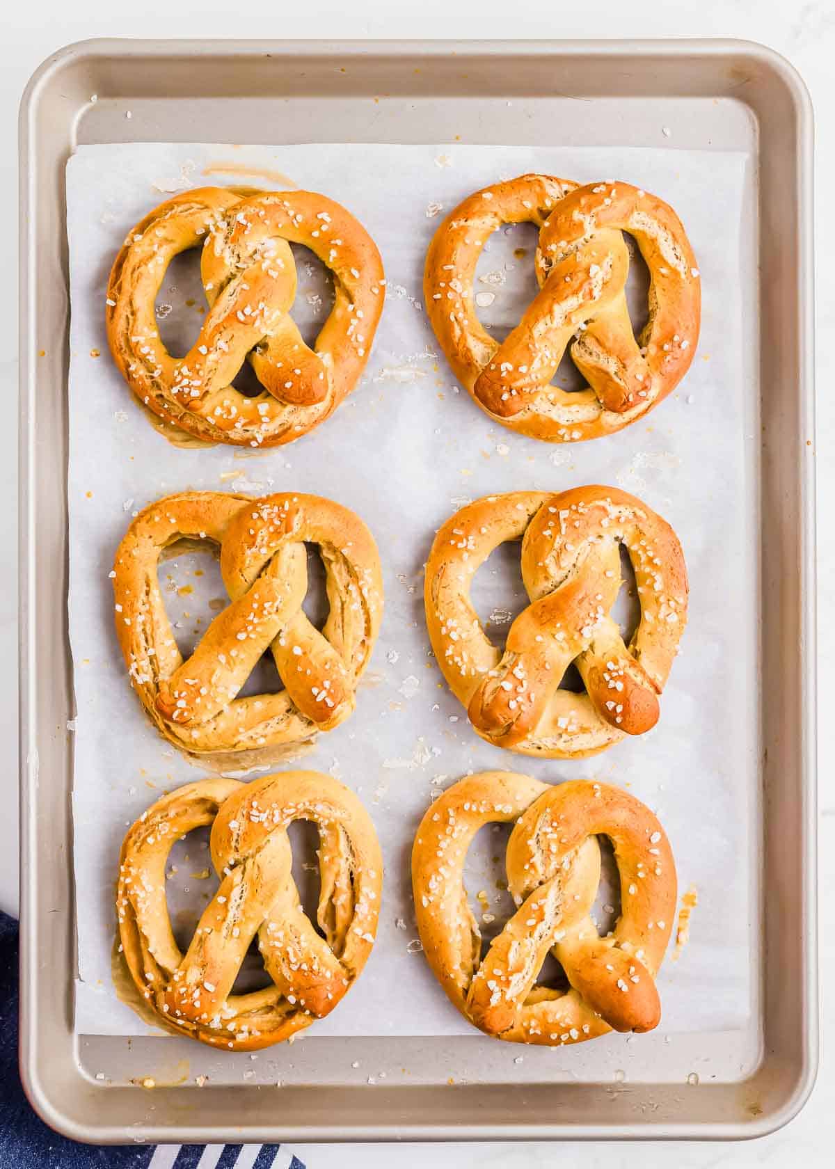 A baking sheet with six freshly baked soft gluten-free pretzels topped with coarse salt.