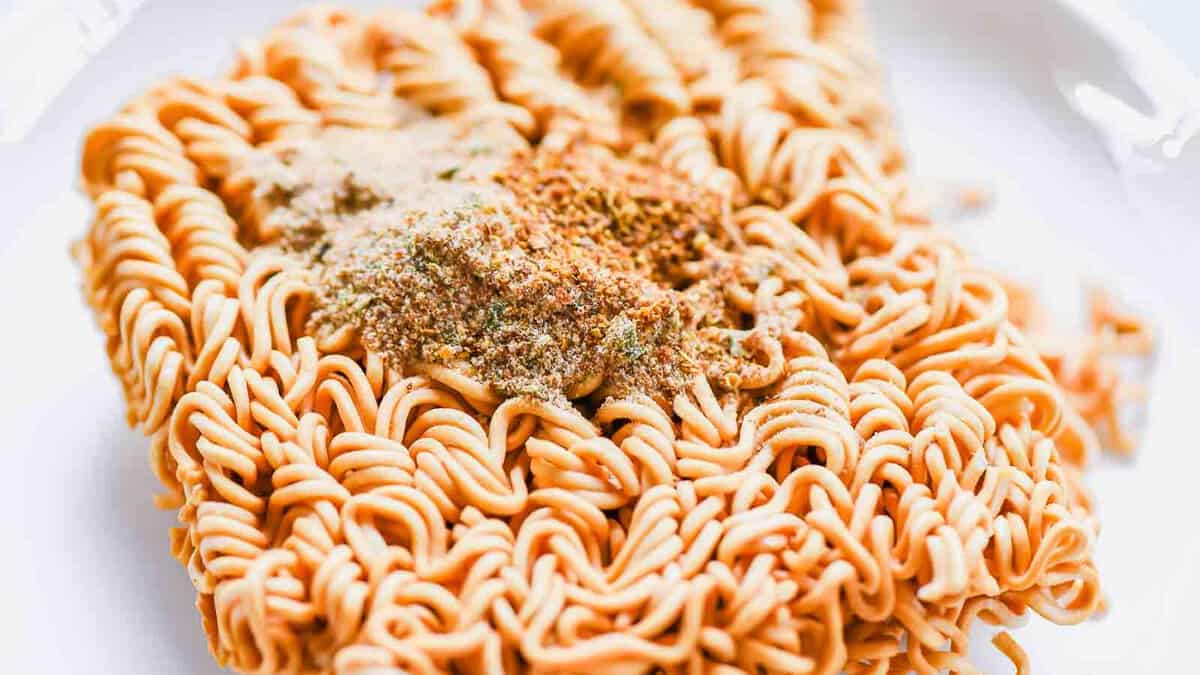 A block of uncooked instant noodles with seasoning powder and dried vegetables sprinkled on top.