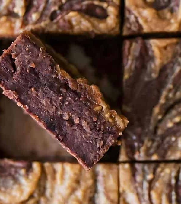 Close-up of a tray of peanut butter swirl brownies, with one brownie lifted out to show the rich, dense layers of chocolate and peanut butter swirls.