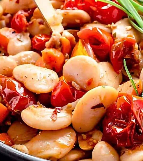 Close-up of a dish featuring butter beans, cherry tomatoes, garlic, and herbs, garnished with sprigs of fresh rosemary.