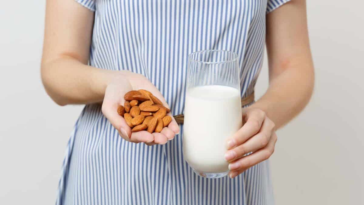 A person in a striped dress holds a handful of almonds in one hand and a glass of milk in the other.