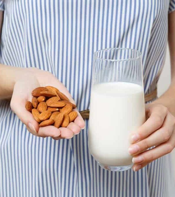 A person in a striped dress holds a handful of almonds in one hand and a glass of milk in the other.