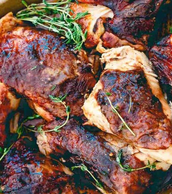 Grilled chicken pieces with a charred exterior on a tray, garnished with fresh herbs and served alongside a small jar of sauce.