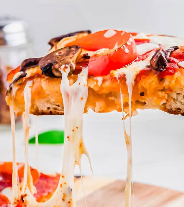 A slice of Blackstone pizza with melted cheese, tomatoes, and mushrooms is being lifted from the rest of the pizza.