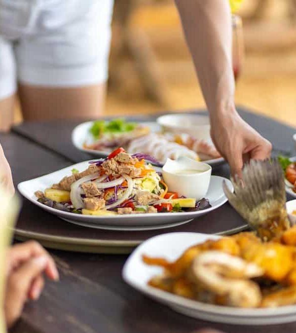 People dining at a table filled with various dishes including salads, shrimp, and fried food. One person is serving food.