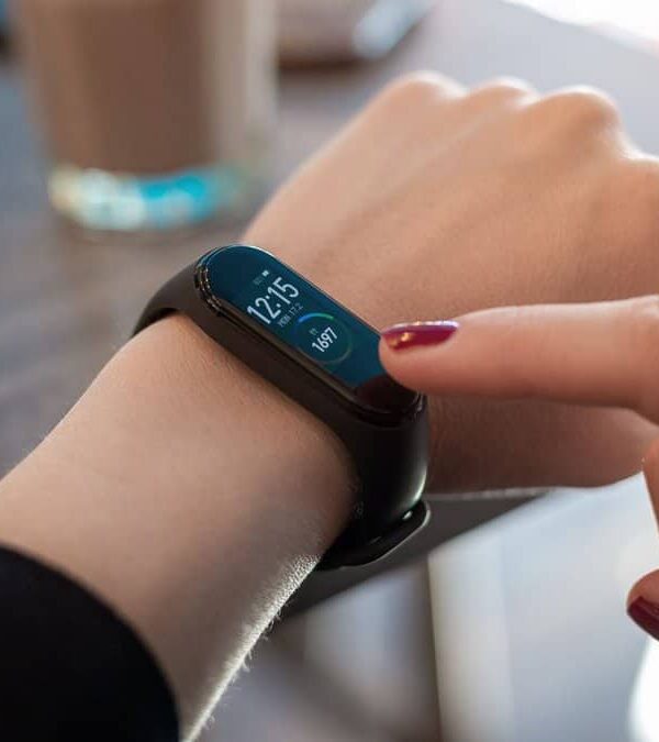 A person taps the screen of a smart fitness tracker on their wrist, displaying the time as 12:15 and a step count of 567.