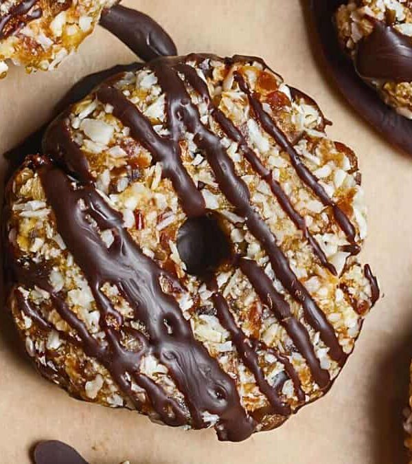 Close-up of several Samoa cookies covered in toasted coconut and caramel, drizzled with chocolate, and placed on a parchment sheet.