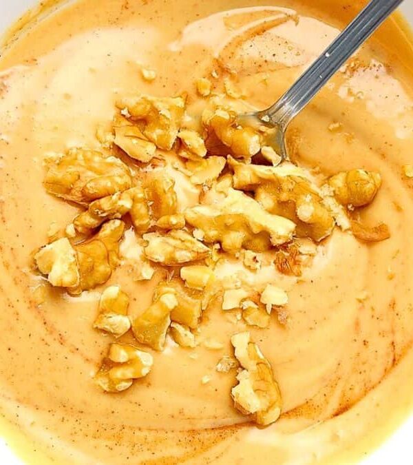A bowl of creamy orange soup garnished with chopped walnuts and a spoon inside the bowl.