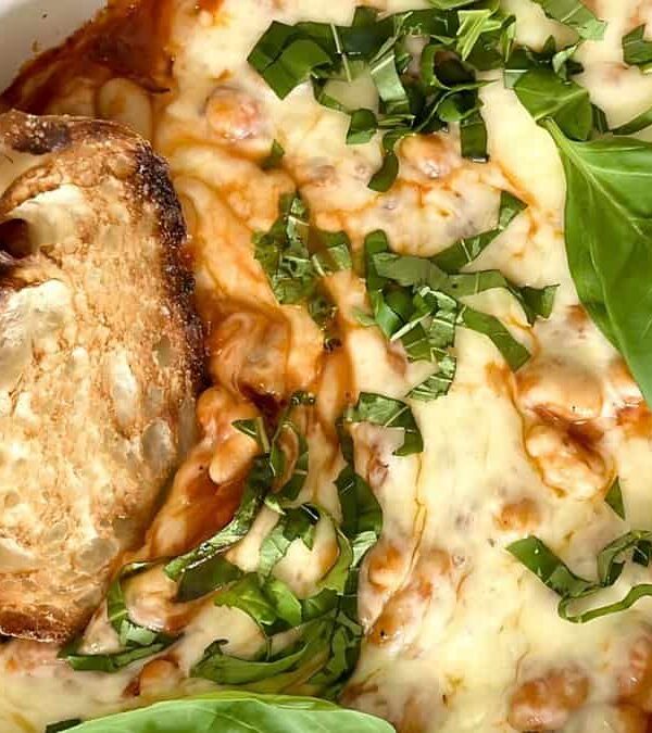 Baked dish with melted cheese, tomato sauce, and fresh basil leaves, served with two slices of toasted bread.