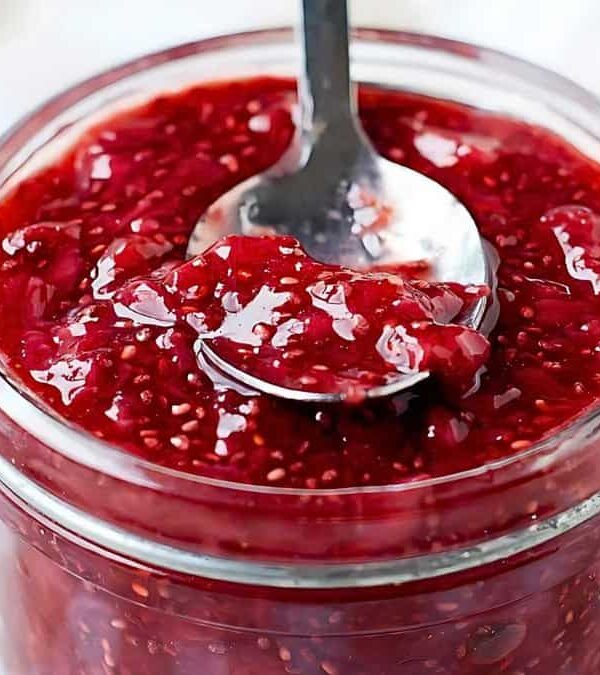 A jar of raspberry chia seed jam with a metal spoon inside.