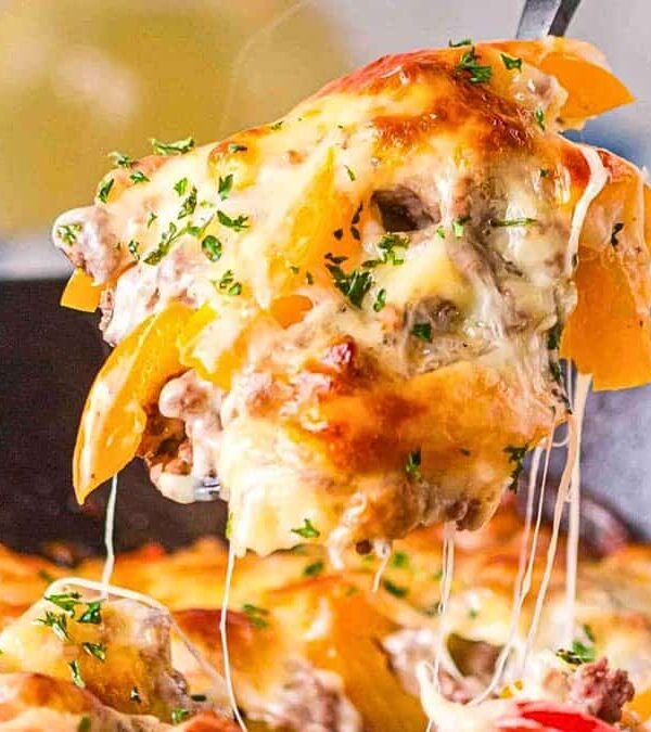 A close-up of a cheesy casserole being lifted from a skillet, showcasing layers of melted cheese, ground meat, bell peppers, and garnished with herbs.
