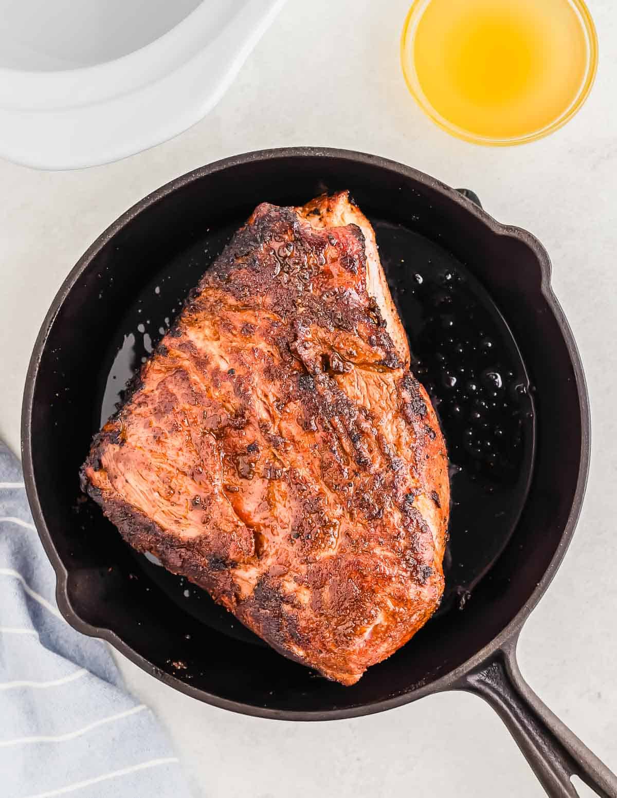 Seasoned and cooked pork roast in a cast iron skillet next to a small bowl of yellow liquid.