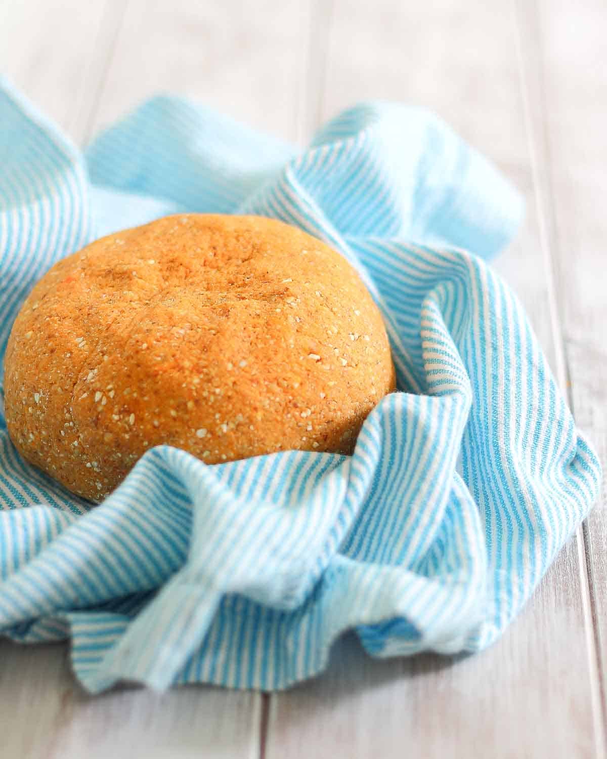 A round shaped dough for making gnocchi on a blue and white striped cloth on a wooden surface.