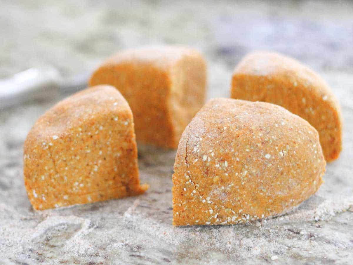 Four pieces of sweet potato gnocchi dough sit on a flour-dusted surface.