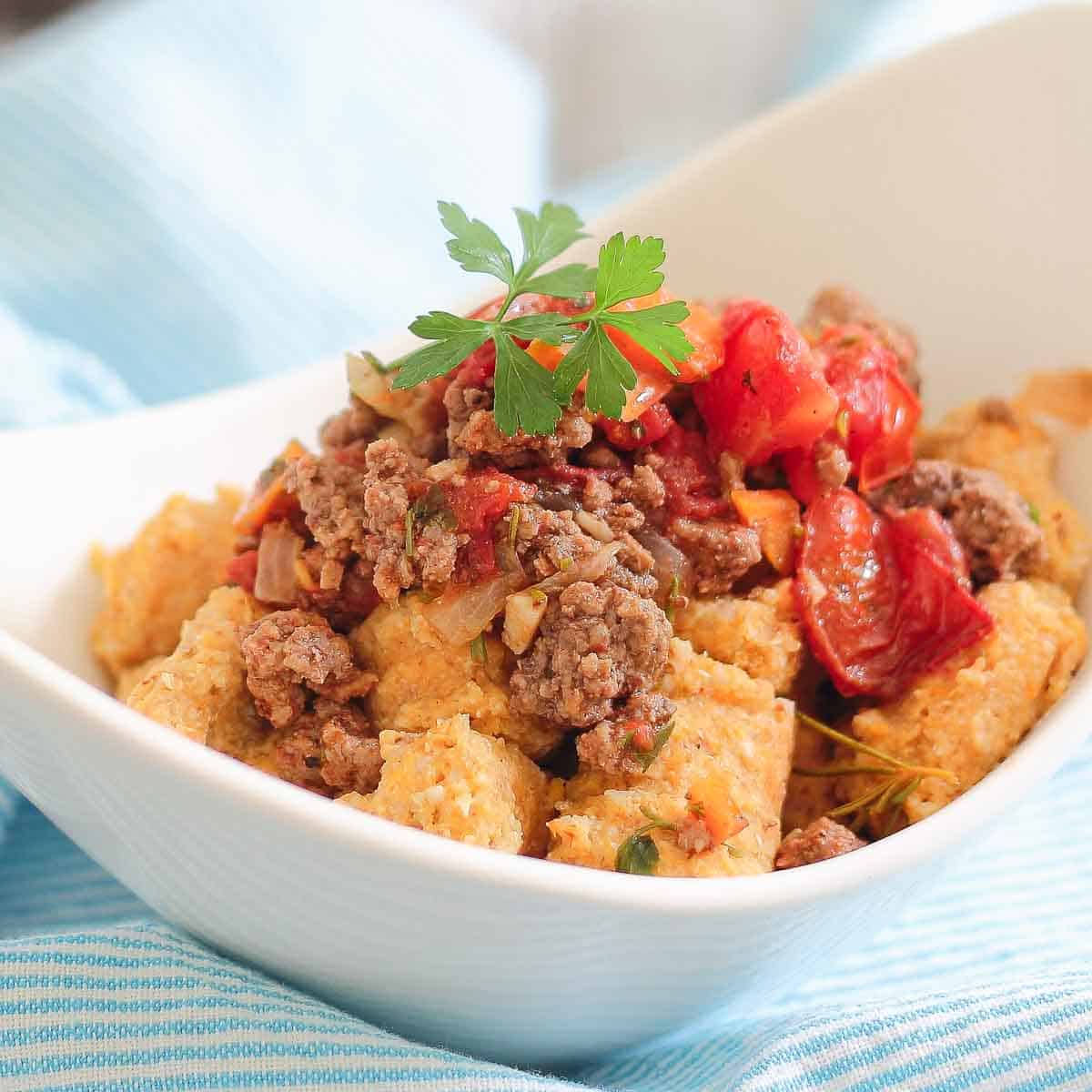 White bowl filled with a dish featuring bolognese meat sauce and sweet potato gnocchi.
