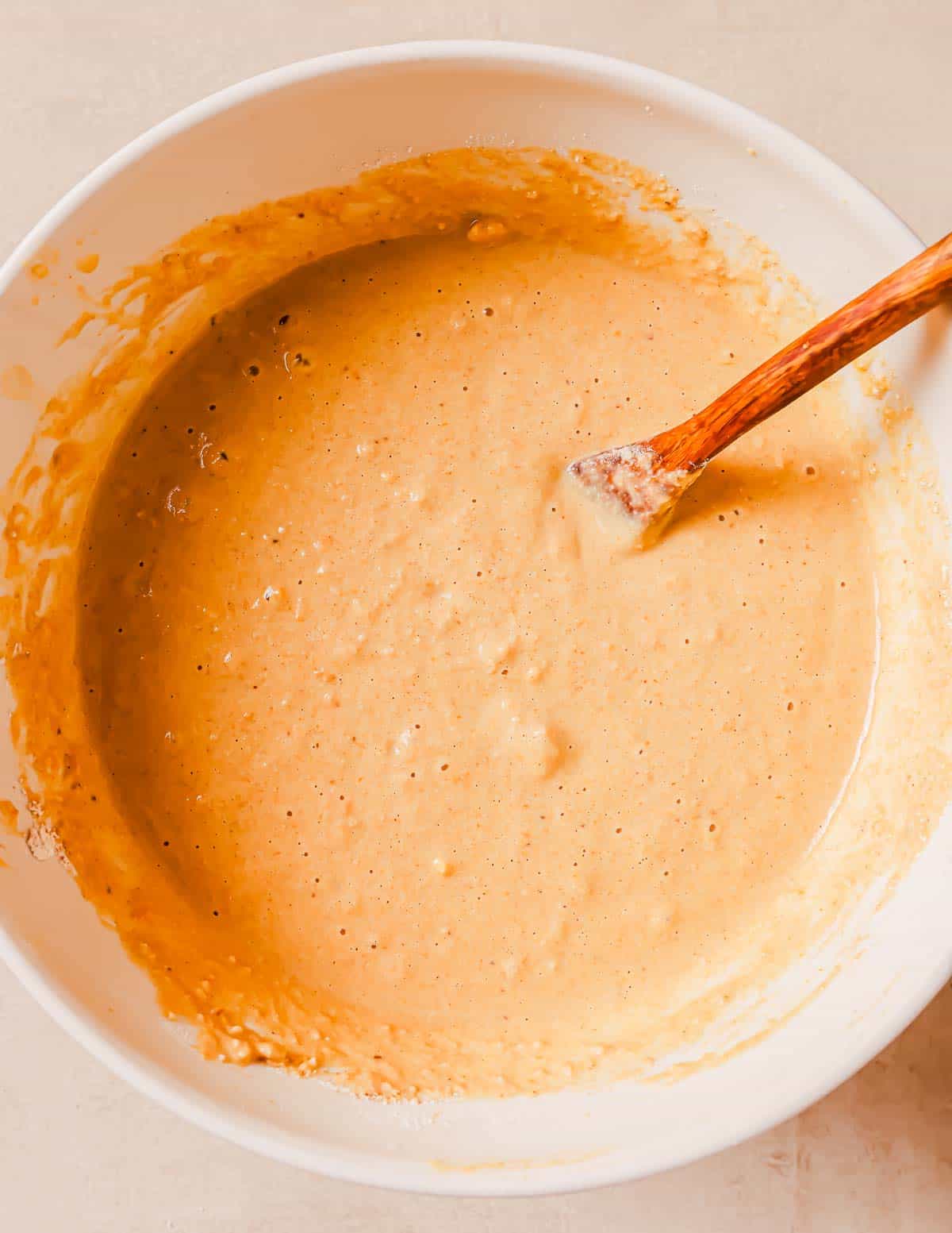 A bowl with a mixture of pancake batter being stirred with a wooden spoon.