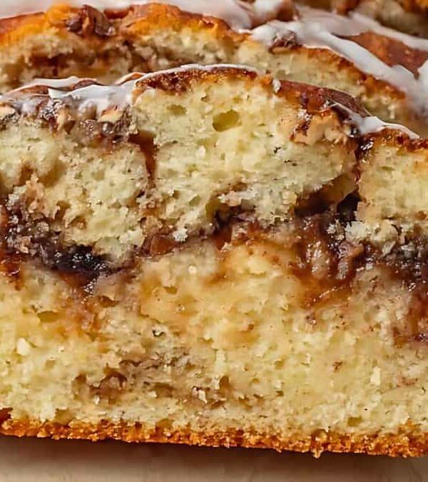 A close-up of a sliced loaf of apple cinnamon bread with a drizzle of icing on top, showing a moist, marbled interior.