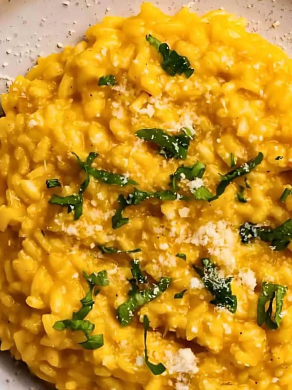 A plate of creamy saffron risotto garnished with grated cheese and fresh parsley. The dish is served on a neutral-colored plate with a light background, creating an appetizing presentation.