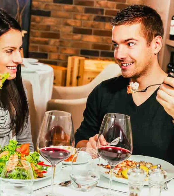 A man and woman sitting at a restaurant table, enjoying a meal with wine.