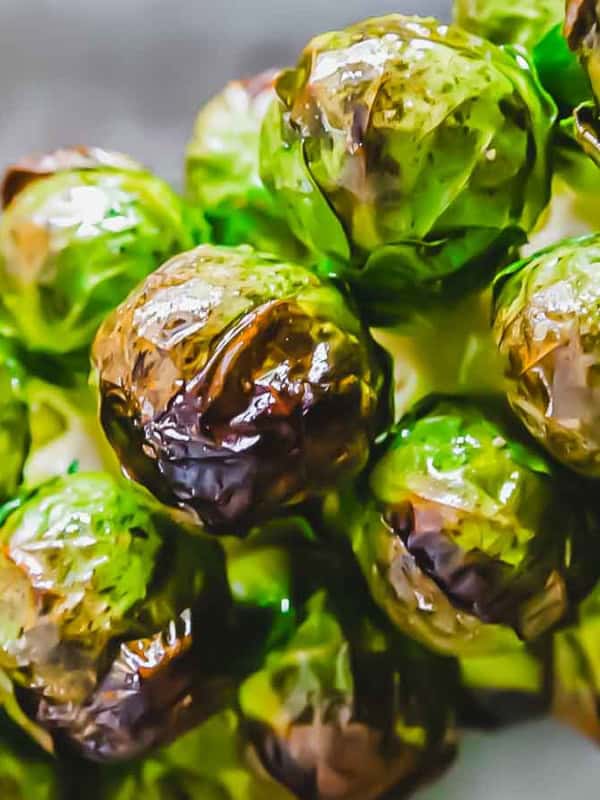 Close-up of roasted Brussels sprouts on a stem, showing a charred and crispy texture. The green and brown colors highlight their roasted appearance.