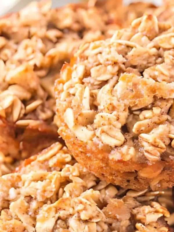 A close-up of baked oatmeal cups topped with oats and nuts, stacked on a white plate. Perfect for cozy apple breakfasts, the golden brown cups look textured and delicious.