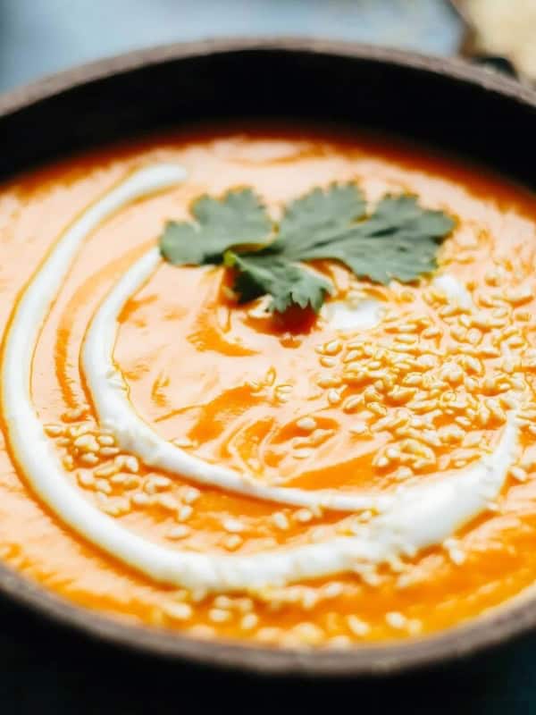 Creamy spicy carrot soup in a black bowl.