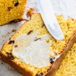 A knife spreading butter on a piece of sweet potato raisin bread.