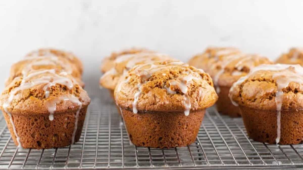 Freshly baked muffins drizzled with glaze are cooling on a wire rack against a light background.