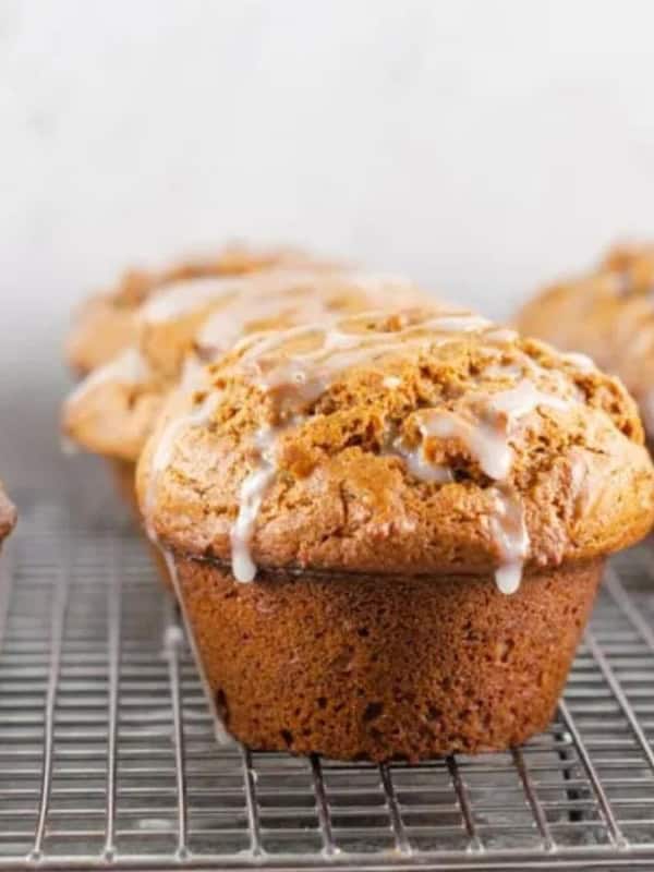 Freshly baked muffins drizzled with glaze are cooling on a wire rack against a light background.