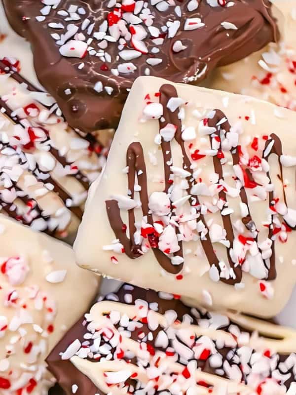 A selection of chocolate-covered rectangular cookies decorated with crushed peppermint candy. Some cookies have dark chocolate drizzle, while others have white chocolate. The crushed peppermint gives a festive, colorful touch.