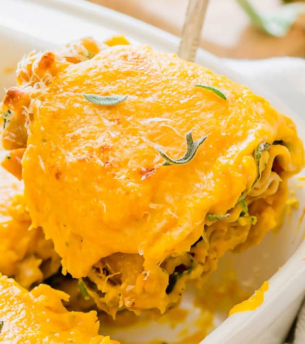 A delicious serving of lasagna rollups is being lifted from a white baking dish. The lasagna is topped with melted cheese and garnished with herbs.
