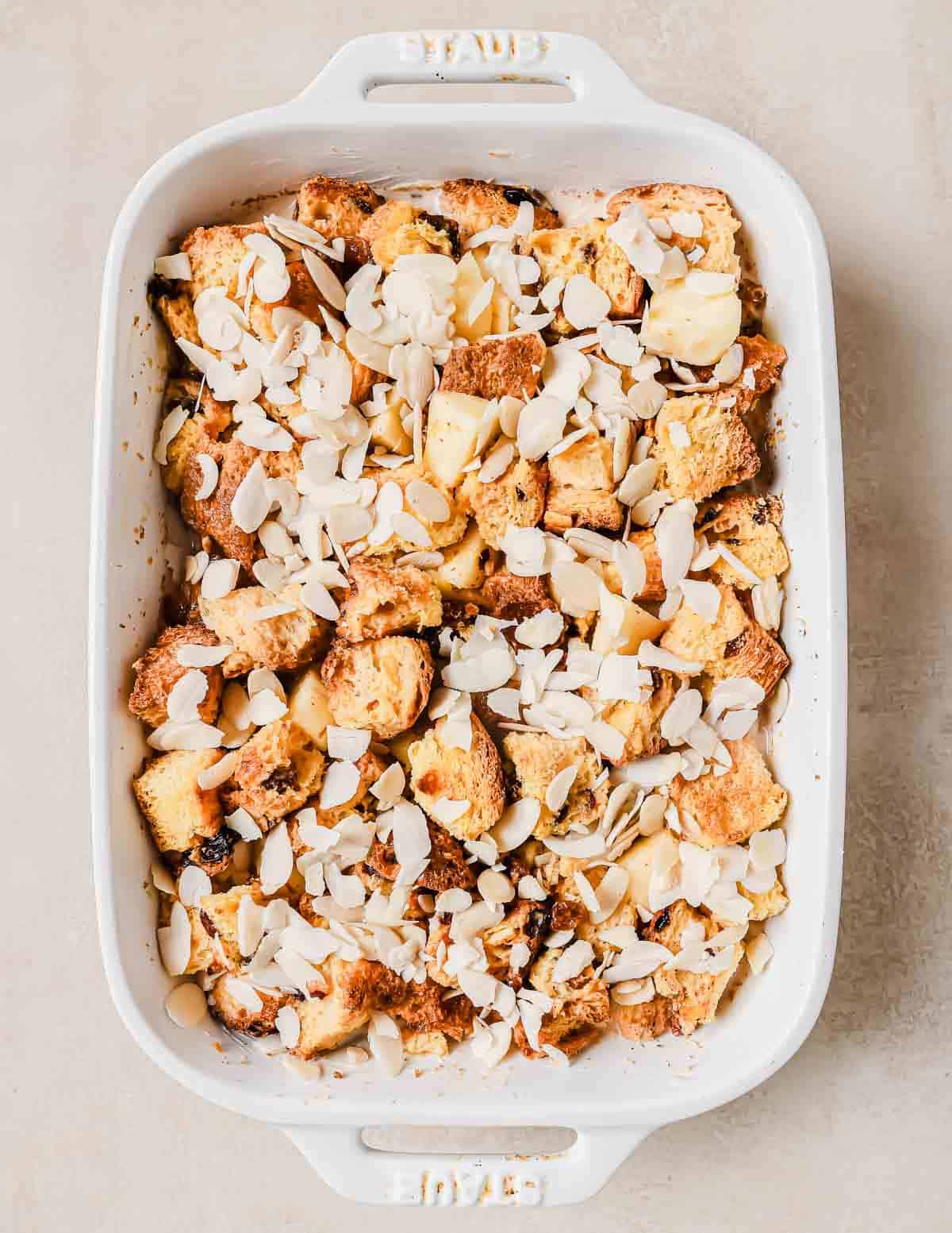 Bread pudding before baking in a white rectangular dish, topped with almond slices. The dish is placed on a light-colored surface.
