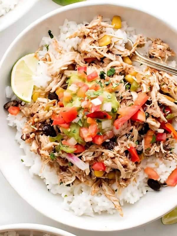 three bowls of shredded chicken with rice, black beans, corn, pico de gallo, and guacamole. There are also lime wedges on the table.