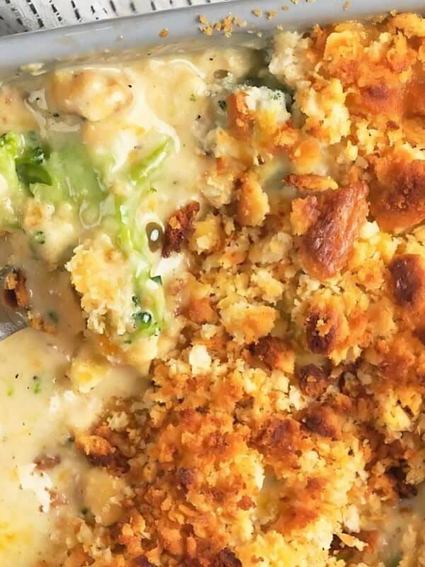 Close-up of a casserole dish filled with a creamy chicken and broccoli casserole. The top is covered with a golden-brown, crumbly crust. A spoon is partially immersed in the dish, revealing the textured filling underneath.