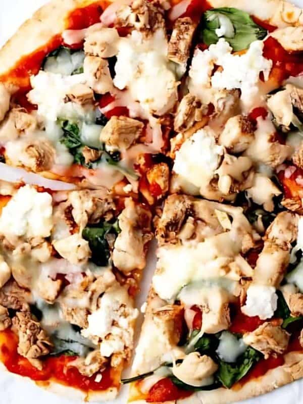 Pizza topped with chunks of chicken, spinach, cheese, and sauce, sliced into six pieces on parchment paper. Nearby are a small bowl of chili flakes, an egg yolk in a dish, and a few fresh spinach leaves.