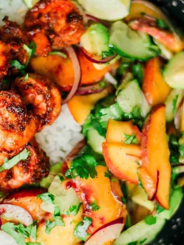 A bowl with shrimp on a bed of rice, topped with a colorful salad of peaches, cucumbers, and onions, garnished with cilantro.