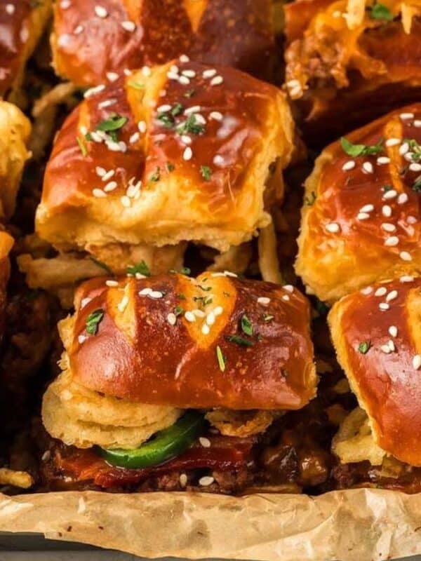 A tray of fresh, golden pretzel slider buns filled with crispy onions, beef, jalapeños, and garnished with sesame seeds. The buns are slightly shiny, and the filling is visible, adding a hearty and savory appeal.