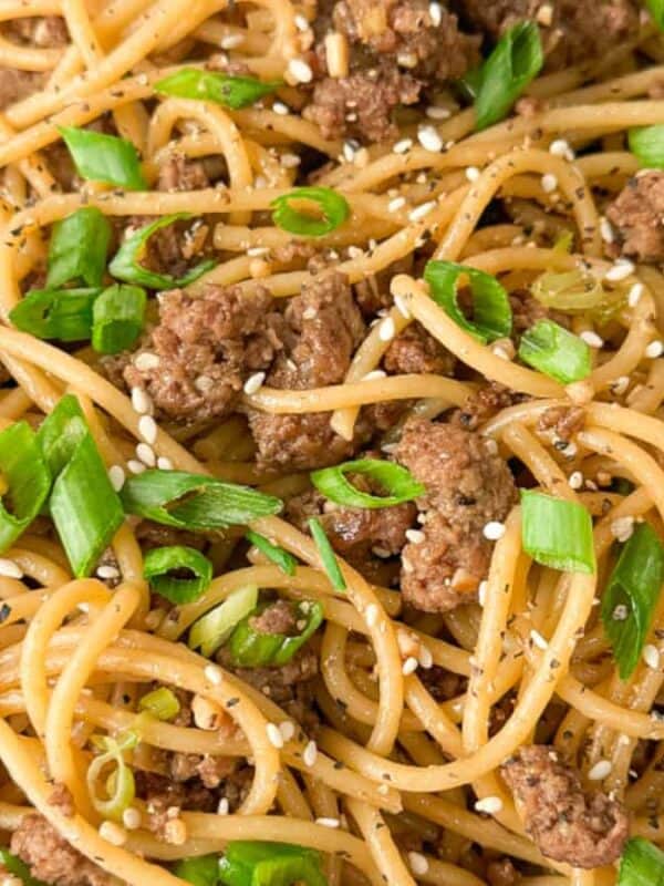 A plate of spaghetti with ground beef, garnished with sliced green onions and sesame seeds. The dish is seasoned with visible black pepper.