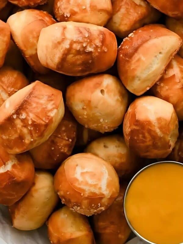 A bowl filled with soft pretzel bites sprinkled with coarse salt, served with a small cup of yellow cheese dipping sauce on the side.
