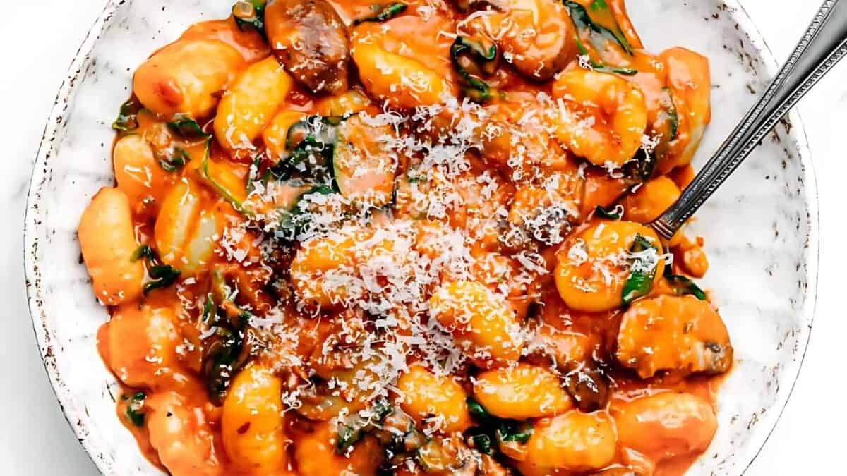 Creamy gnocchi in a rich tomato sauce with spinach and mushrooms, topped with grated parmesan cheese, served on a white plate.